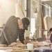 Two artisans create custom-made wood furniture in a workshop where the sun shines through the window.