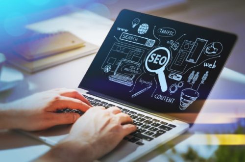 Businessman working on a laptop with SEO icons sketched on the screen and other marketing buzzwords.