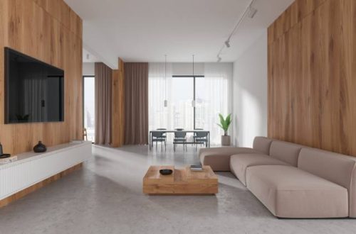 Modern living room with large windows in the background, brown furniture, concrete stained floors, and a large tv screen.