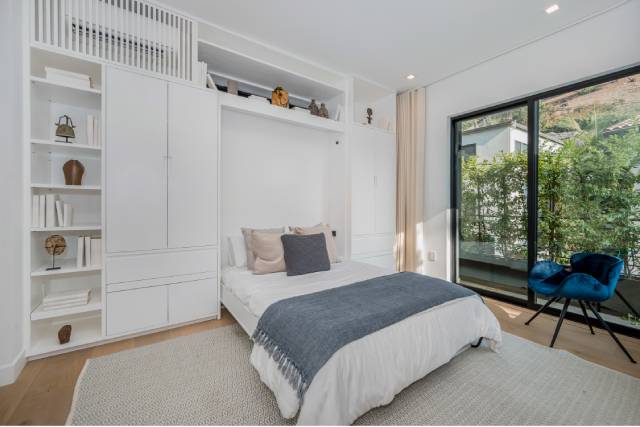 White, built-in shelves and cabinets with decorations are above and on both sides of a made Murphy bed.
