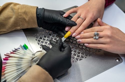 A nail salon owner and tech working with a client to measure their nail size. They're practicing with a yellow nail swatch.
