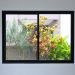 A sliding glass window with a black frame features a view into a backyard with vibrant greenery and a fence.