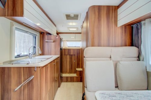 An interior view of a well-appointed RV. The decor includes a wood-paneled kitchenette and plush seating area.