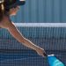 A female pickleball player on the court going after the ball with her paddle and arm stretched out. She's wearing a visor.