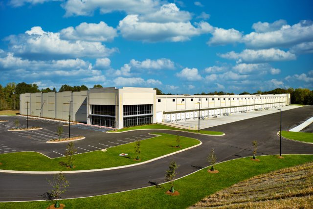 The exterior of a large white office building with an empty parking lot. There is a loading dock on one side of the building.