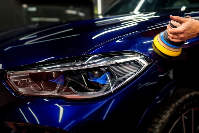 A blue used vehicle in the auto body shop. A car mechanic is working with an electric buffer to polish the paint.