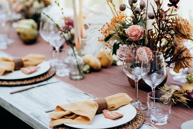 A wedding reception tablescape with tall taper candles, wine glasses, and earth tone floral arrangements in the center.