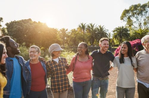 Smiling multigenerational adults standing side by side outdoors with their arms wrapped around each other.
