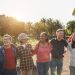 Smiling multigenerational adults standing side by side outdoors with their arms wrapped around each other.