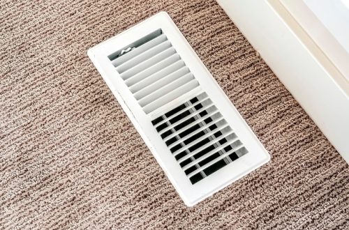 A close-up shows a white air vent cover that is surrounded by brown carpet with white and black specks.