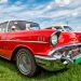 A red and white classic Chevrolet vehicle, with chrome details, parked on grass under a bright blue sky.