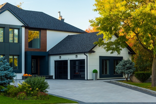 A two-story modern home features a large mature tree, a concrete driveway, and a meticulously cared-for lawn.