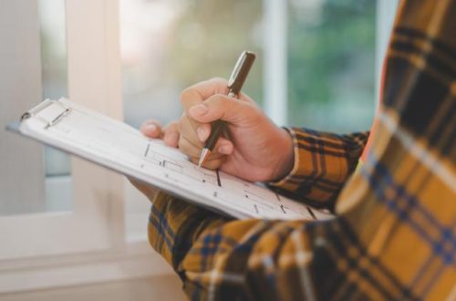 A person in a flannel shirt is writing down notes on a piece of paper that’s on a clipboard.