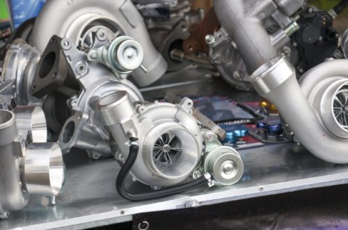 The silver components of the inside of a vehicle engine, featuring a turbocharger in the front.
