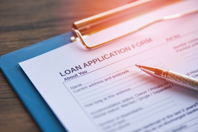 A close-up of a pen resting on a clipboard with a blank Loan Application Form attached in a warm lighting.