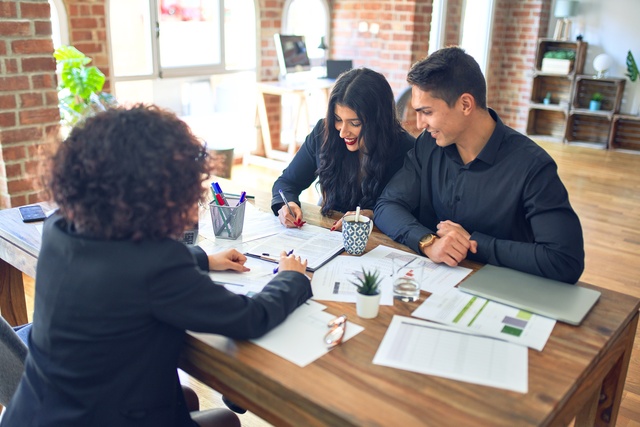 A couple sits at the desk in the lender's office as they review mortgage underwriting decisions with the lender.