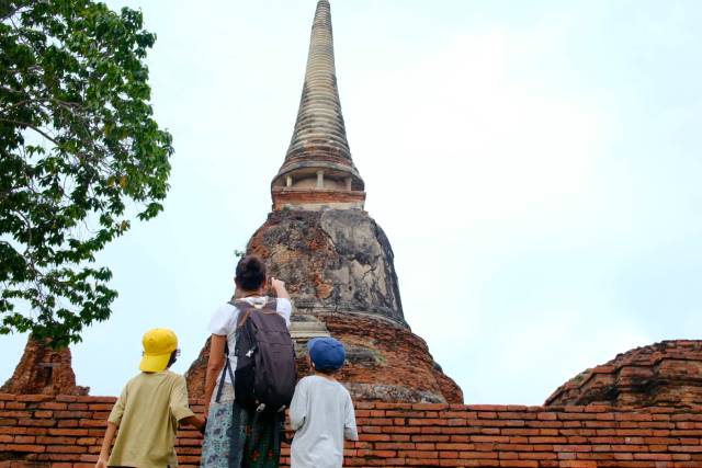 Two young students stand next to an adult teacher as the teacher points to a monument on a field trip.