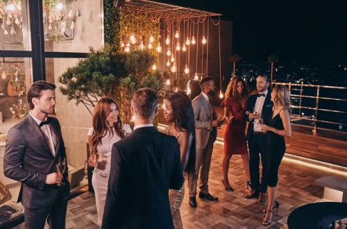A group of people gathered around at an event on a lit-up patio. They're wearing semi-formal attire.