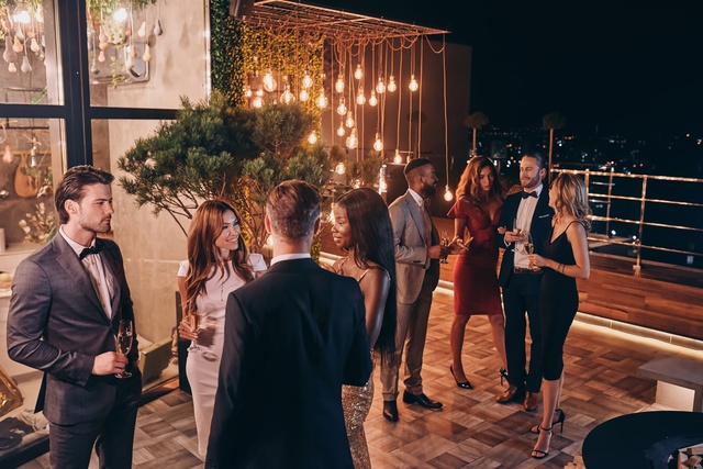 A group of people gathered around at an event on a lit-up patio. They're wearing semi-formal attire.