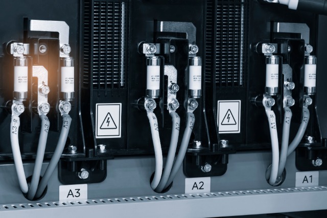 Gray cables connected to labeled A1, A2, and A3 terminals inside a black electrical panel with warning icons.