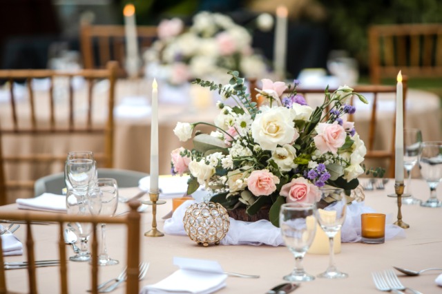 A romantic wedding table with lush pink and white floral centerpiece, taper candles, glassware, and elegant place settings.