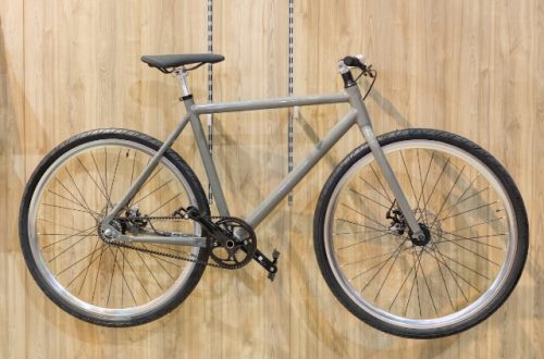 A plain, gray bicycle is hanging horizontally on metal hooks that are attached to a wooden wall.
